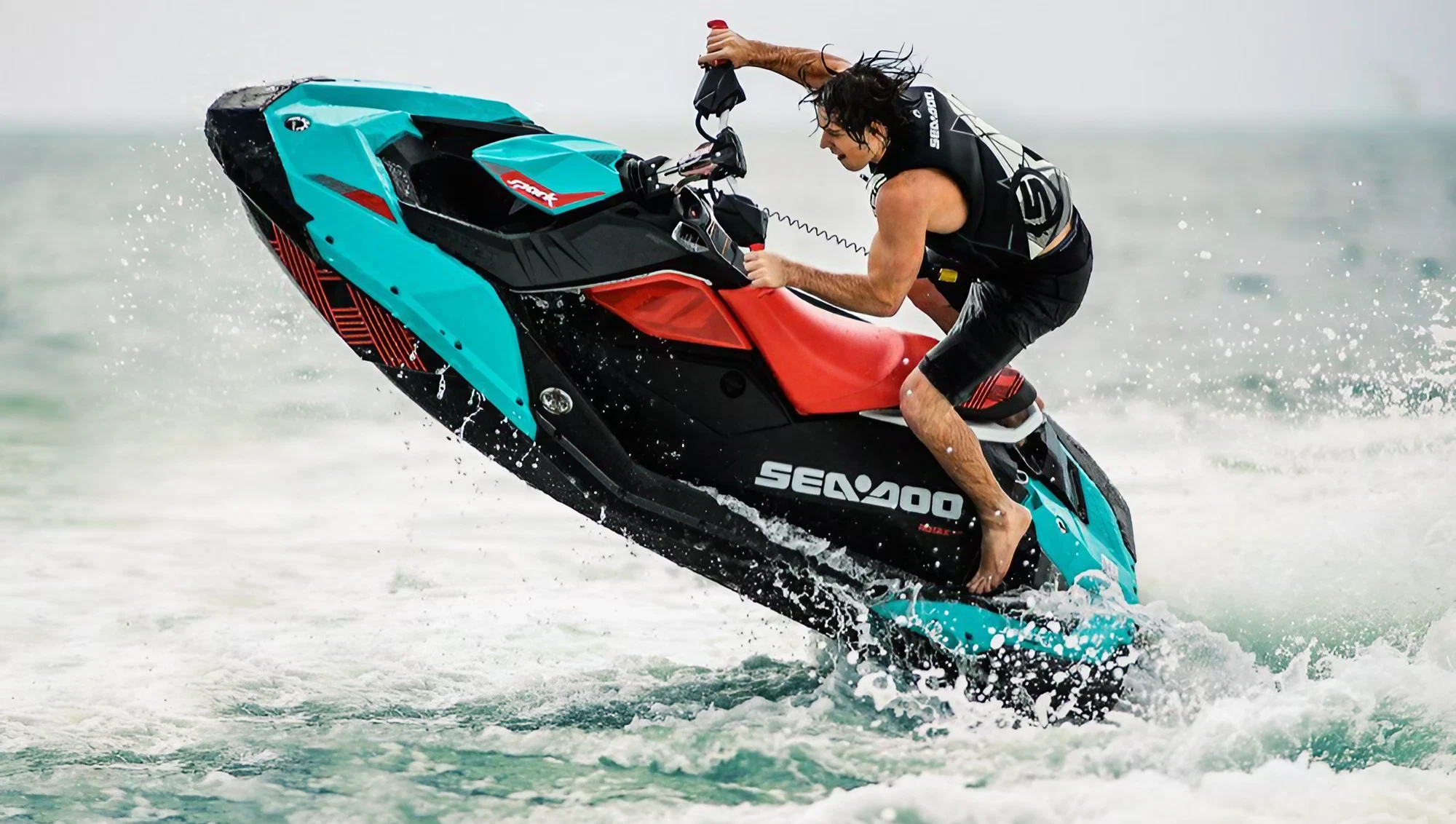 Rider jumping a turquoise jet ski over a wave